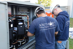 Southport Heating, Plumbing, and Geothermal technicians Josh Pothast (left) and Nicholas Draeger (right) install a 30-ton Modine Atherion rooftop packaged unit.