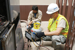 HVAC specialists A1C Samuel Groover and Roy Matsuoka digitally monitor refrigeration weight and pressure of a chiller in order to correctly recharge the unit.