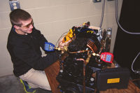 Figure 1. A student service technician sets up an ammeter and Bluetooth high- and low-side pressure gauges on a compressor after fixing a leak near the liquid line solenoid valve and charging refrigerant to a glass door reach-in freezer. 