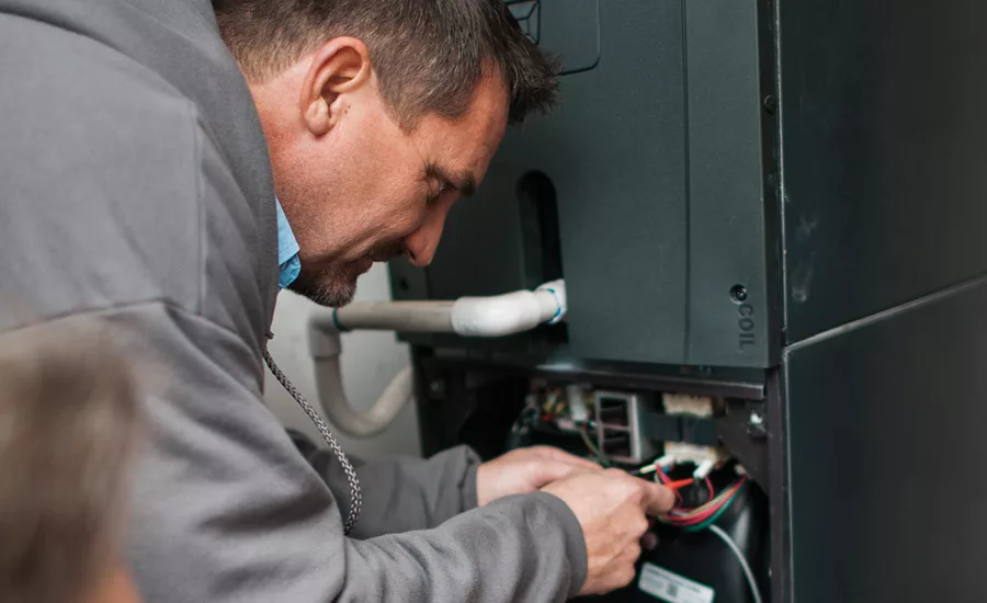 Les Dorsett, service technician for Sky Heating & Air Conditioning in Portland, holds a multimeter while Mike Herbert, installation manager, works on a Trane system.