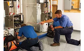 Betlem Heating technicians Zach (left) and Miles practice troubleshooting furnaces in the company’s training lab under the watchful eye of their trainer, Andy (center).