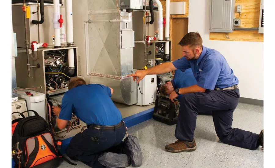 Betlem Heating technicians Zach (left) and Miles practice troubleshooting furnaces in the company’s training lab under the watchful eye of their trainer, Andy (center).