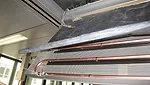 Close-up of radiant ceiling panel components: metallic ceiling panel, coil, thermal insulation and stainless steel flexible connectors.